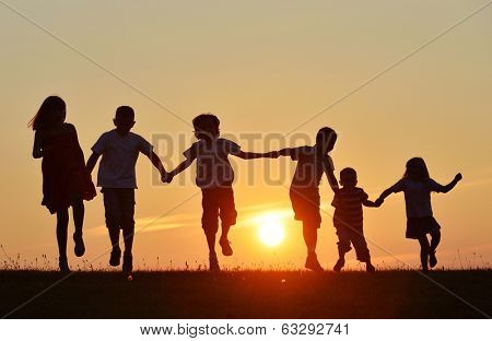 Happy children silhouettes on summer meadow running and jumping