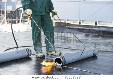 Roofer installing Roofing felt with heating and melting of bitumen roll by torch on flame during roof repair