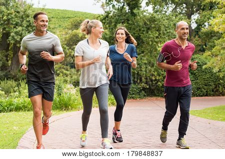 Healthy group of people jogging on track in park. Happy couple enjoying friend time at jogging park while running. Mature friends running together outdoor.