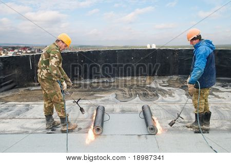 Roofing felt installation with heating and melting roll of bitumen roll by torch on flame