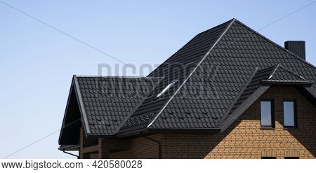 Brown Corrugated Metal Profile Roof Installed On A Modern House With A Attic Windows. The Roof Of Co