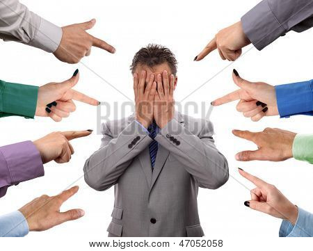 Hands pointing towards businessman holding head in hands concept for blame, accusations and bullying