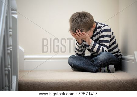 Upset problem child with head in hands sitting on staircase concept for bullying, depression stress or frustration