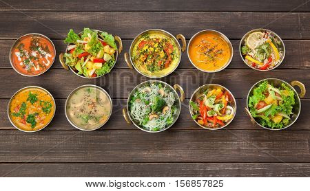 Vegan or vegetarian restaurant dishes top view, hot spicy indian soups, rice and salads in copper bowls. Traditional indian cuisine meal assortment on wood background. Healthy eastern local food