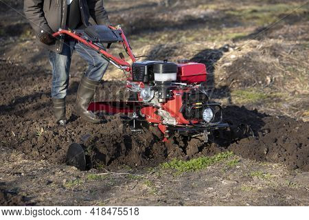 A Farmer Man Plows The Land With A Cultivator. Machinery Cultivator For Soil Cultivation In The Gard