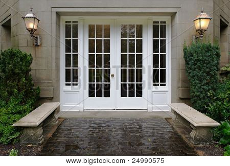 Elegant stone walkway bordered by stone benches leading to a double glass paned front door with two large front lanterns