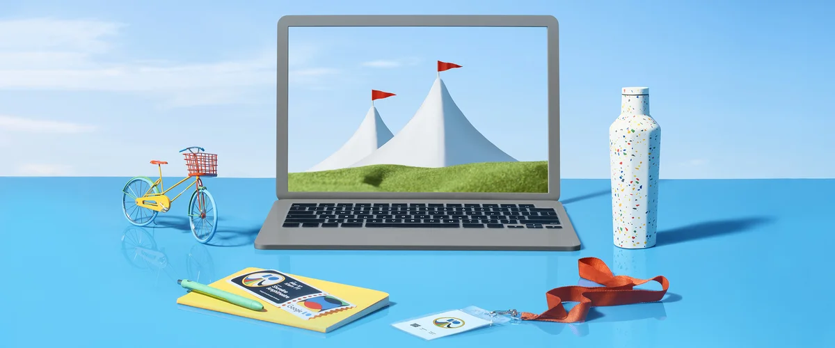 Illustration of an open laptop sitting on a blue table. There are two large tents with flags on the laptop screen next to a green field. On the blue table, there is a Google event badge, a water bottle, a notepad and pencil and a cruiser bicycle with red,