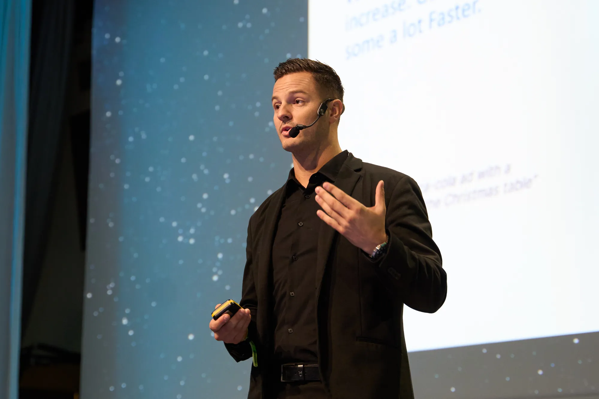 A man in a black suit looks stands in front of a screen.