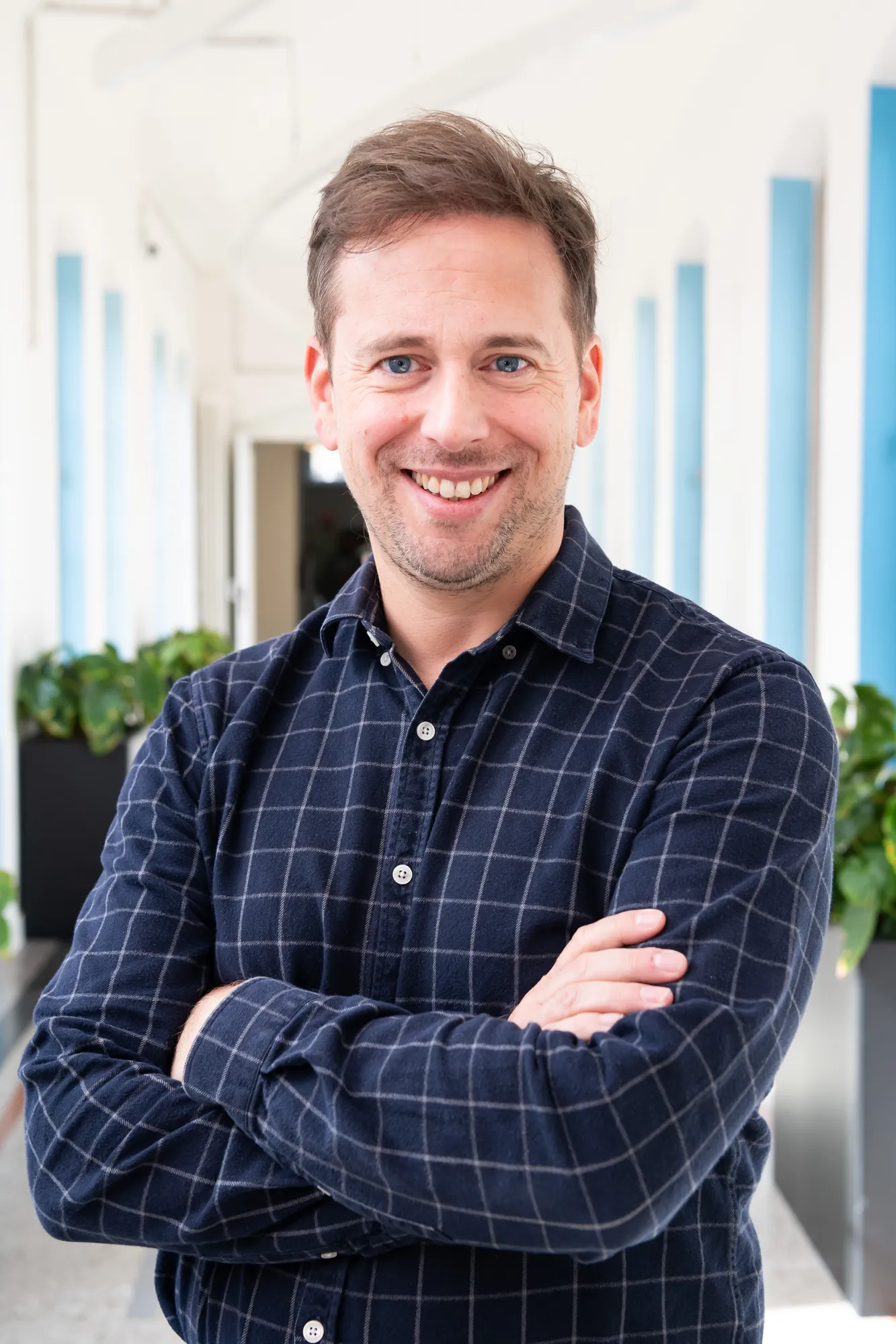 A man wearing a blue shirt stands with his arms folded looking at the camera.