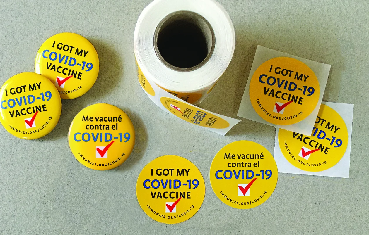 Image of yellow stickers and pin-back buttons with “I got my COVID-19 vaccine” written in English or Spanish.