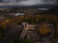 It’s a dark and mysterious photograph. In the center we can see ruins of Chojnik Castle. There are trees inside the courtyard of the castle. Behind the castle we can see two small lakes and some clouds on the horizon. The photograph was taken after dusk, most likely during early autumn.