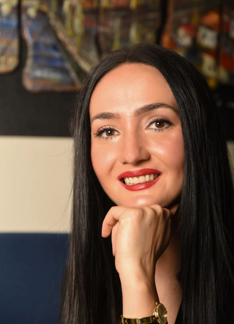 A woman with long black hair smiles at the camera, with her hand propped up underneath her chin.