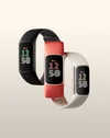 Three Fitbits in various colors, black, coral, and porcelain, all floating against a neutral background