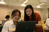 Two young women sharing a black laptop in a classroom setting