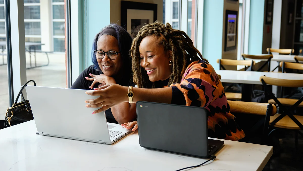 Two people sitting at a table smiling and looking at a laptop screen together.