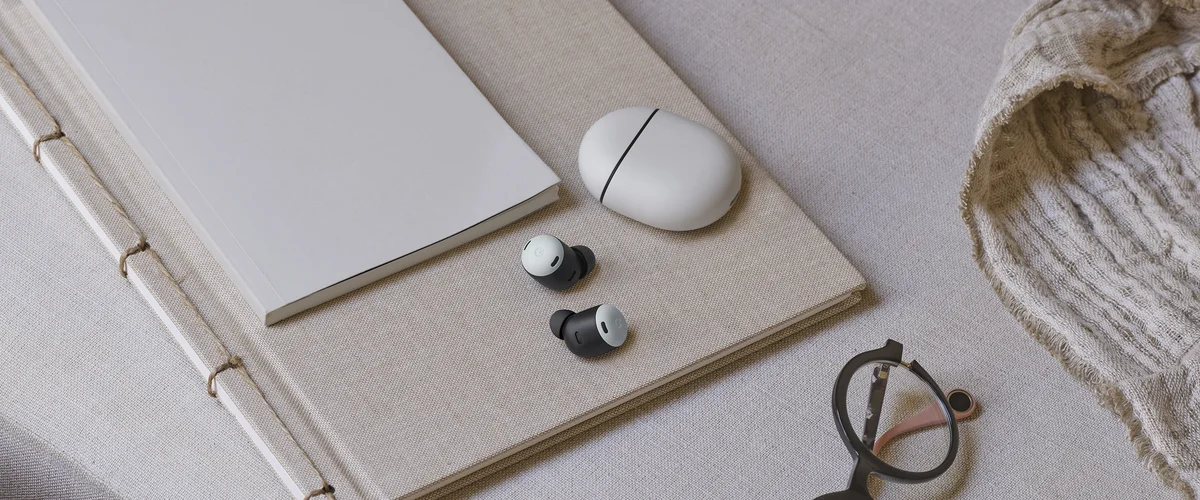 A pair of Pixel Buds Pro sit on a notepad with the case next to them.