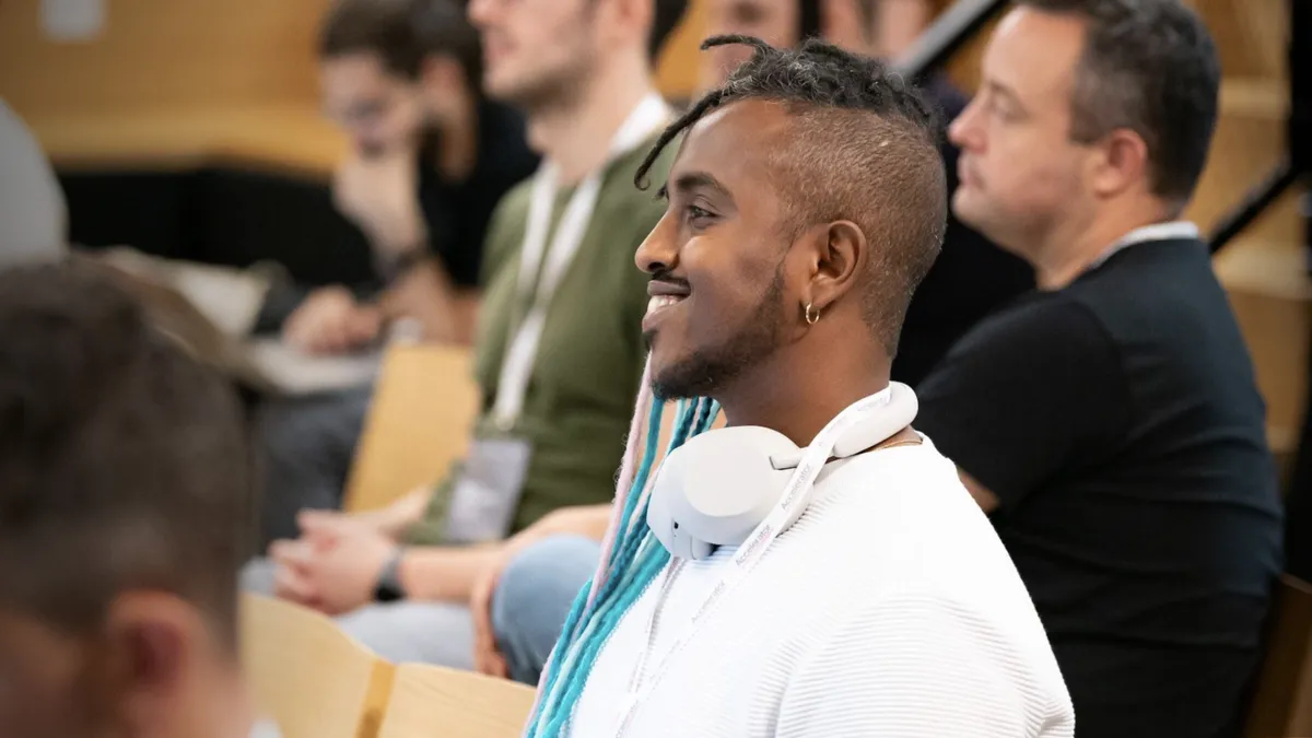 A man wearing a white shirt and white headphones looks across the room, between people on either side.