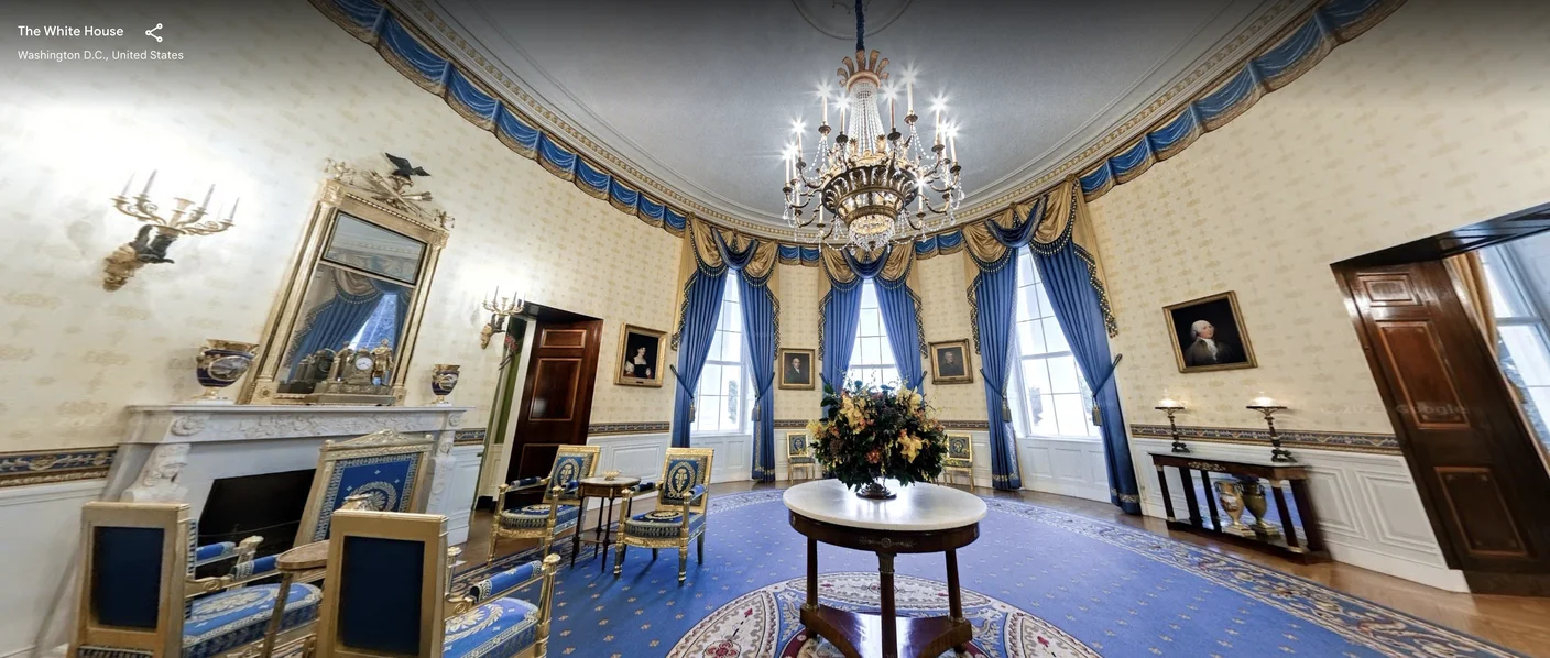 The blue room in the White House. Blue carpet and blue drapes are in a room with paintings on the wall and a chandelier hanging from the ceiling.