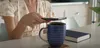 Photo of a person sitting at a table holding a Pixel phone over a coffee mug.