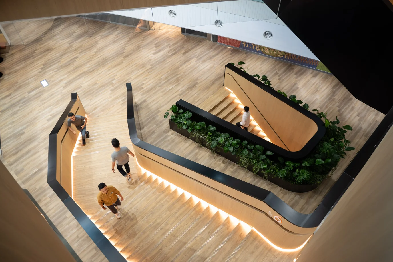 A birds eye view of a wooden sculptural staircase with three people standing on it.