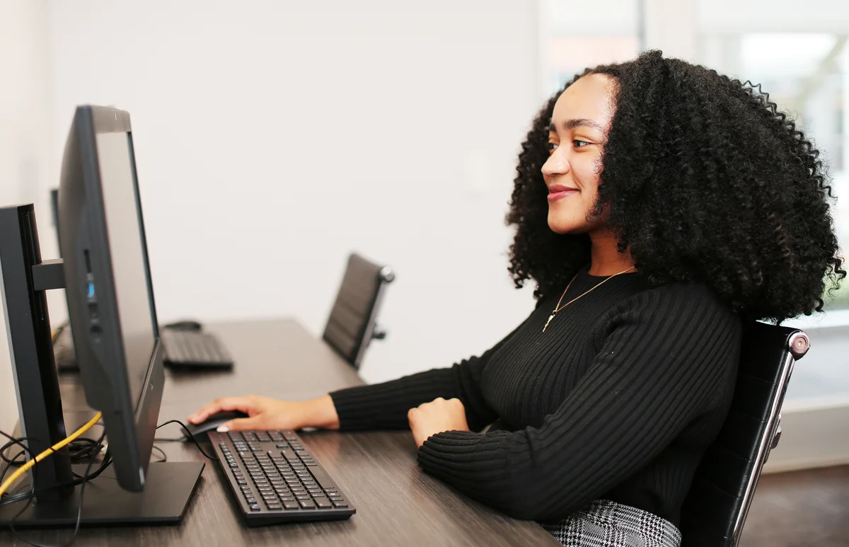 A young, smiling woman sits at a computer in front of a sunny window at the University of Georgia's cybersecurity clinic.