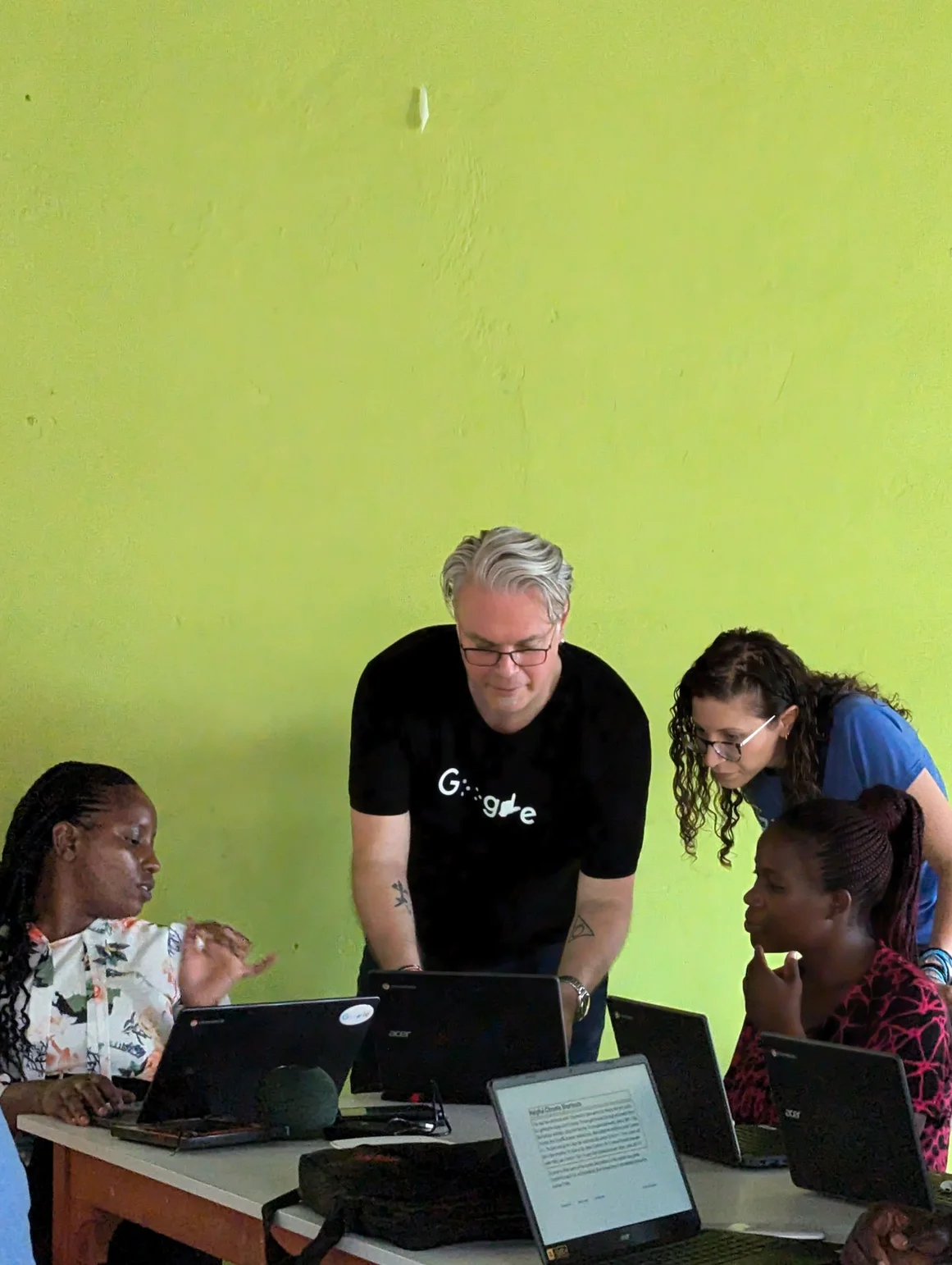 Two Googlers stand and talk to a seated teacher from Kenya