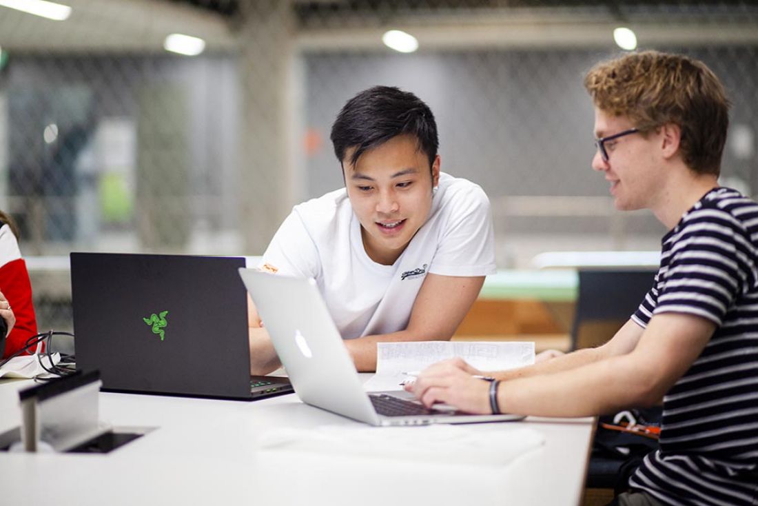 A male student looks at his laptop with male staff helping