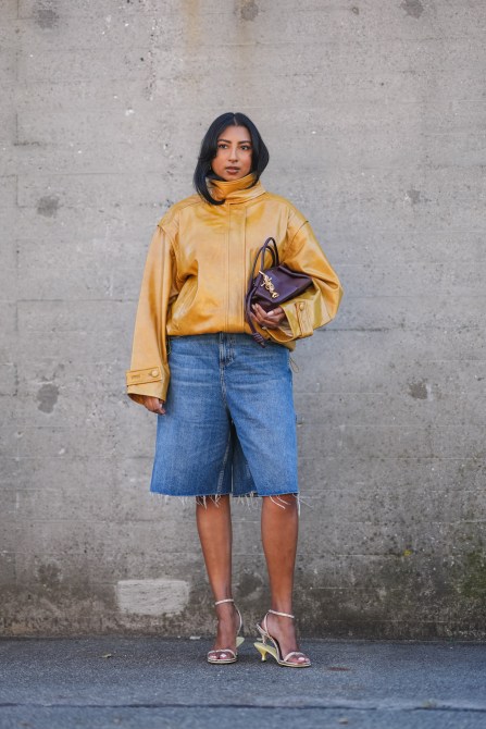 COPENHAGEN, DENMARK - AUGUST 06: A guest wears a brown shiny leather jacket with puff sleeves, a burgundy leather bag, blue ripped denim / jeans shorts / jorts, kitten heels shoes, outside Remain, during day two of the Copenhagen Fashion Week (CPHFW) SS25 on August 06, 2024 in Copenhagen, Denmark.