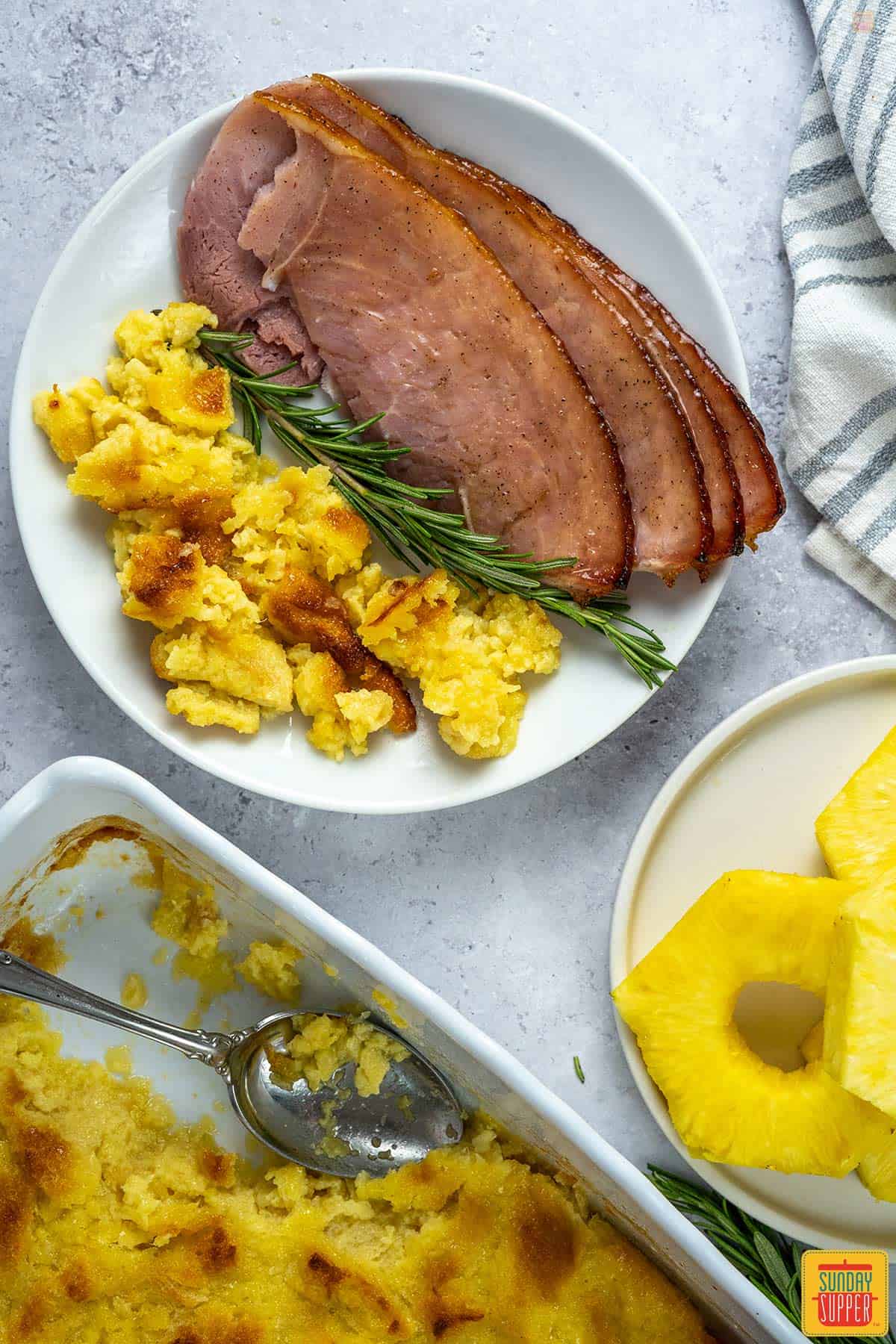 slices of honey glazed ham on a plate with pineapple casserole