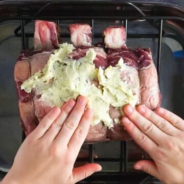 hands pressing prime rib seasoning on to a prime rib