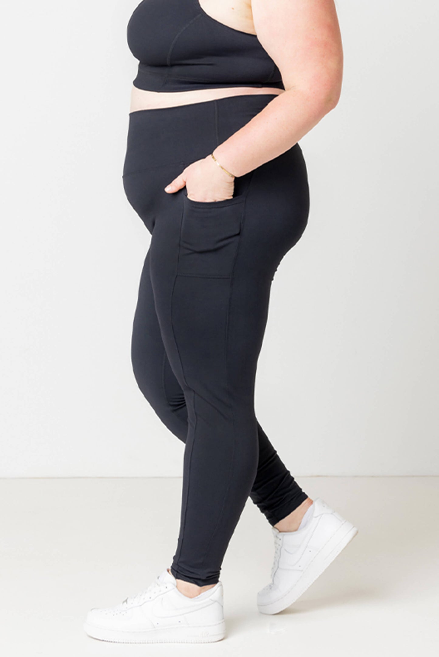 Profile view of model walking in Superfit Hero plus size pocket ankle leggings