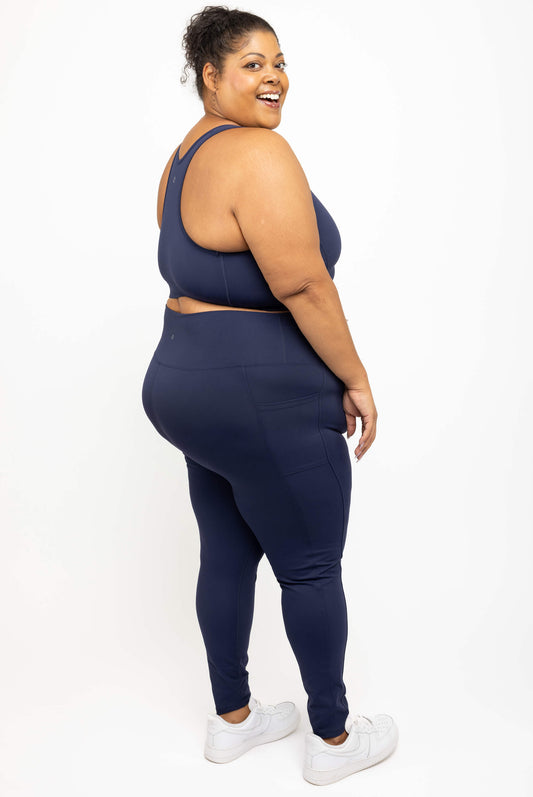 Model looking over her shoulder wearing Superfit Hero plus size compression leggings with pockets in navy size 3X