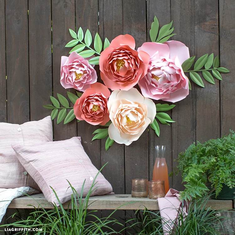 Paper peonies in various sizes on a wooden fence.