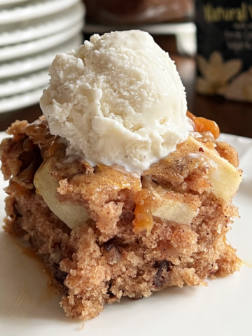 This image shows a piece of Fresh Apple Crazy Cake on a plate with a scoop of vanilla ice cream on top.