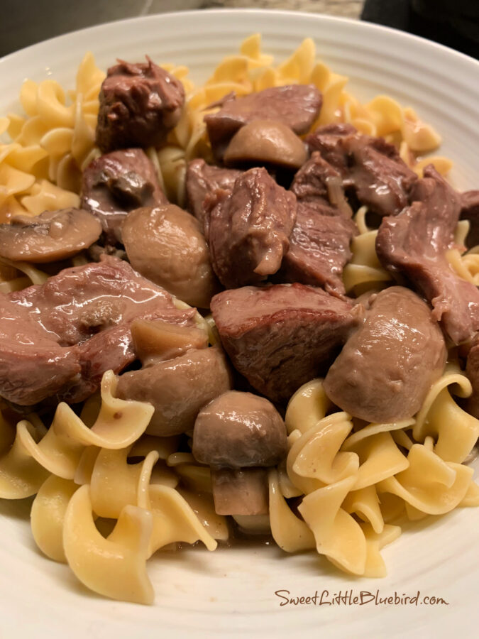 Slow Cooker Smothered Beef Tips and gravy over egg noodles in a white serving bowl