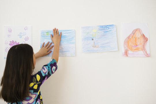 Mixed race girl hanging drawings on wall