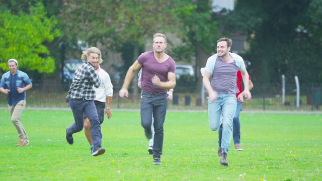  Happy energetic young male friends playing rugby or American football in the park