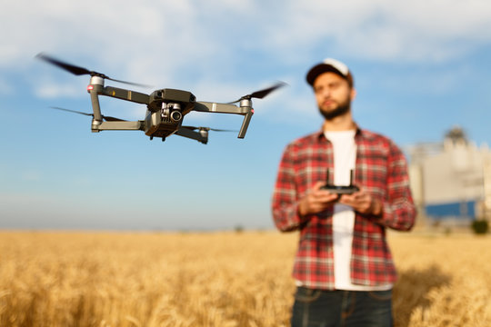 Compact drone hovers in front of farmer with remote controller in his hands. Quadcopter flies near pilot. Agronomist taking aerial photos and videos in a wheat field