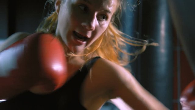 A girl is a boxer. The girl is training in the boxing hall. The girl is beating a punching bag.