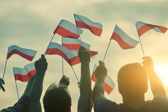 Poland patriots, back view. People raising polish flags up to the sky.