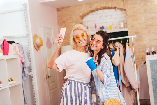 Coffee and photo. Smiling daughter drinking coffee making photo with modern mother while shopping together