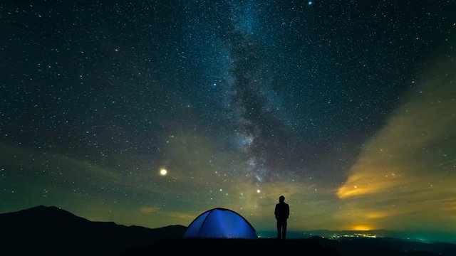 The man near camping tent standing on a meteor shower background. time lapse