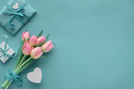 Springtime turquoise paper background with pink tulips and wrapped gifts, copy-space