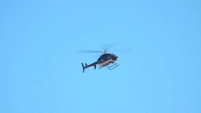 A modern, unmarked helicopter hovers in the sky at an angle, as viewed from the ground.