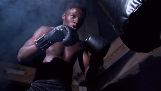 Sportsman training his fist hitting boxing bag low angle close up shot in smoke