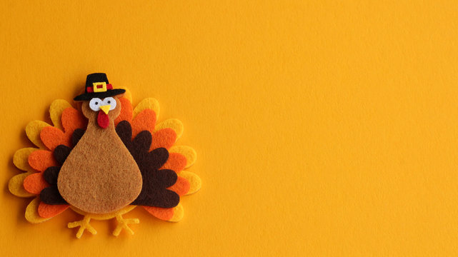 orange brown and yellow crafted felt turkey laying flat on an orange background with copy space	