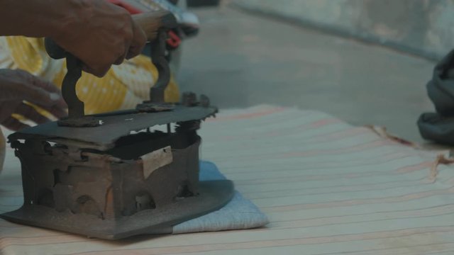 an indian man ironing his shirt with a very old and rusty iron symbolizing that India is still a developing country