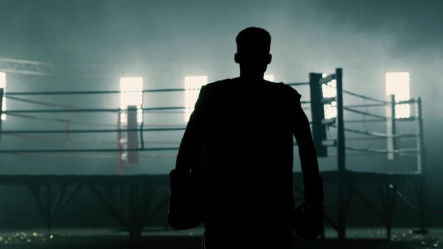 Dramatic silhouette of a boxer walking towards a boxing ring in slow motion.