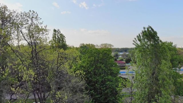 Aerial footage of a park in Bucharest, Herastrau, summer, with green trees and blue sky and a lake, slow rise of drone footage in Romania, Europe with people.