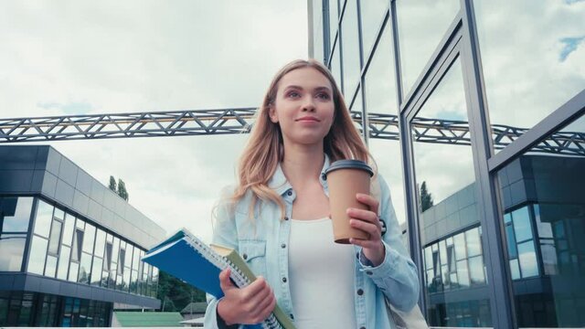 Smiling student drinking coffee to go while walking on urban street